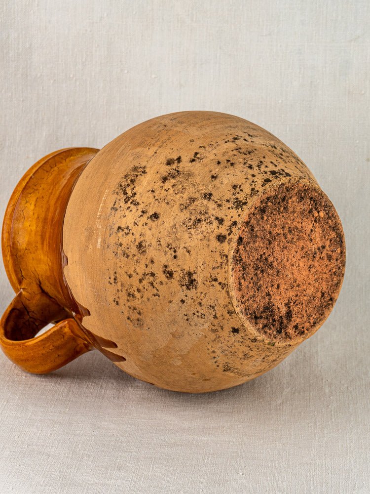Vintage French Aubagne terracotta pitcher with amber glaze, textured base, and single handle.