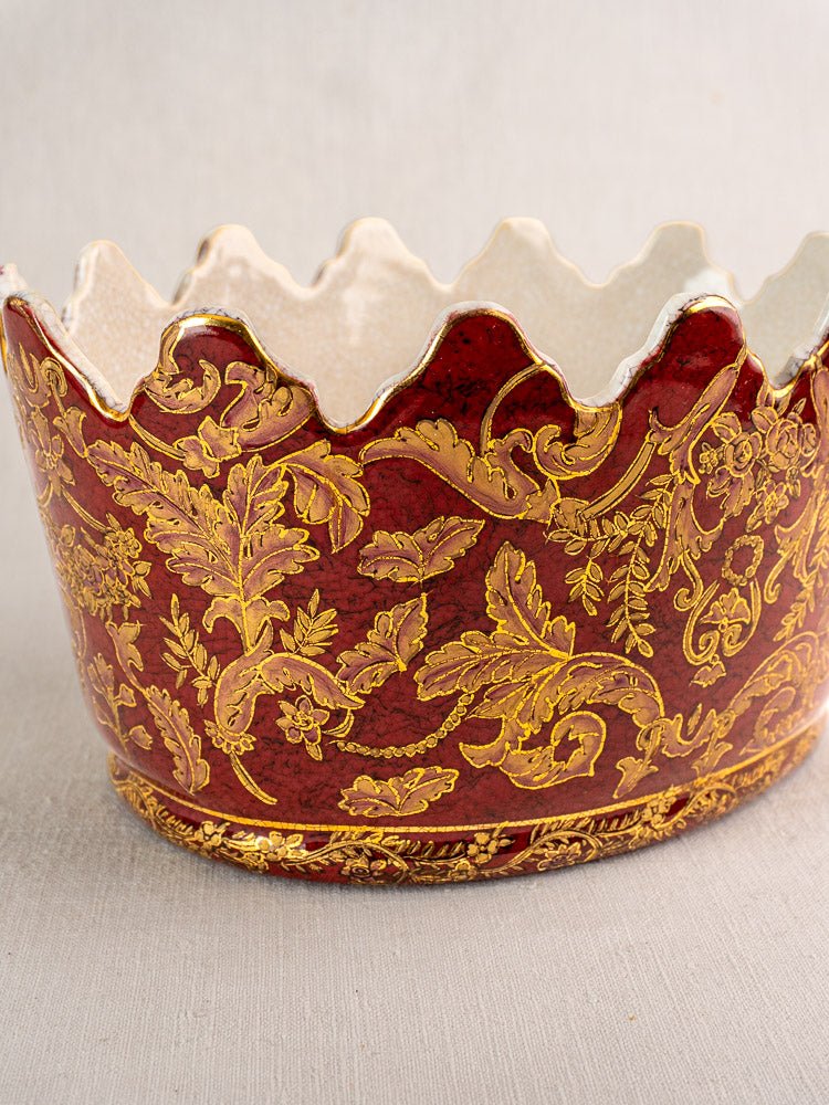Antique French ceramic wine cooler with scalloped edges and gold floral motifs on neutral surface.