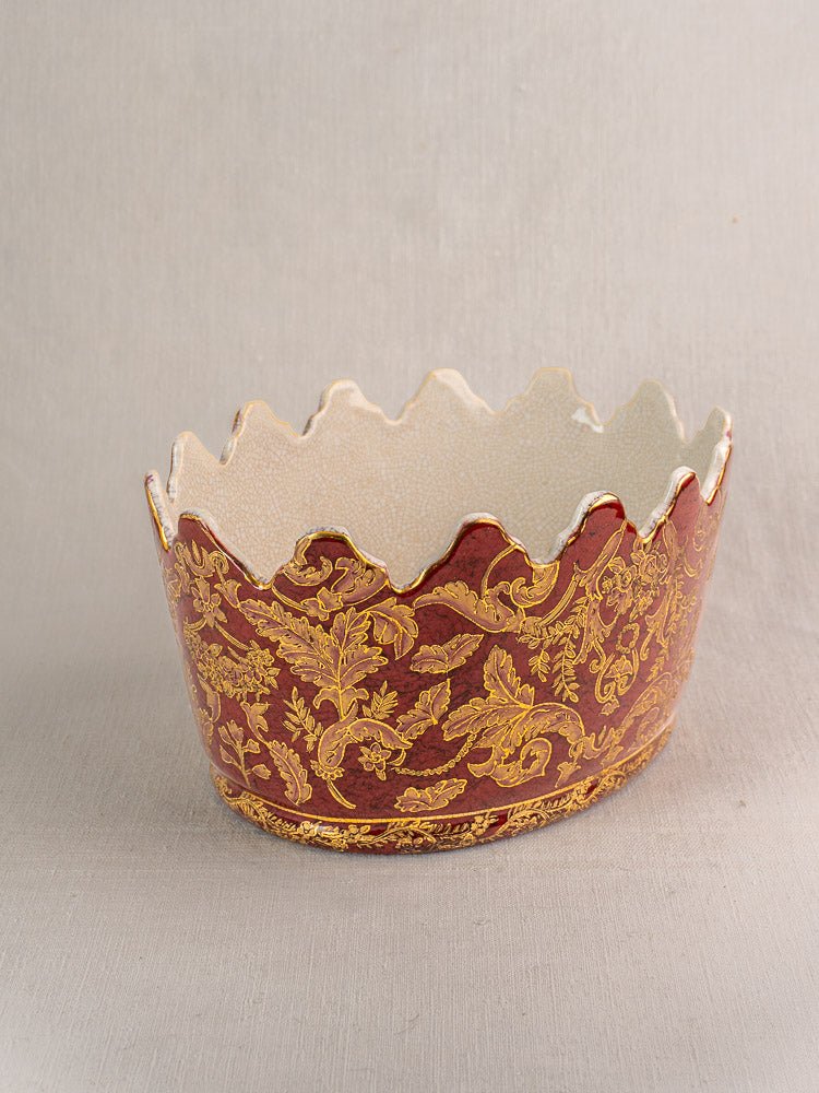 Antique French Terre de Fer rafraîchissoir with jagged rim and gold floral motifs on red, on fabric.