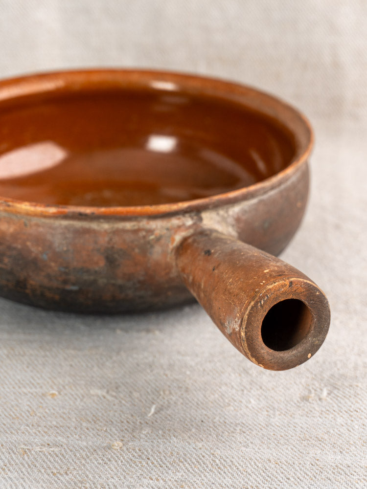 Antique French Saint-Uze stoneware poêlon with rustic brown glaze and spout on neutral fabric.