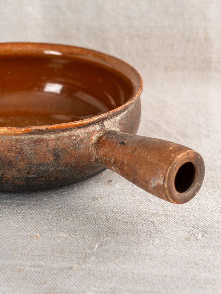Antique French Saint-Uze marked stoneware cooking pan with rustic brown ceramic finish on beige fabric.