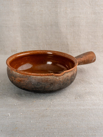 Antique French Saint-Uze stoneware poêlon with brown glaze, handle, and spout on gray cloth.