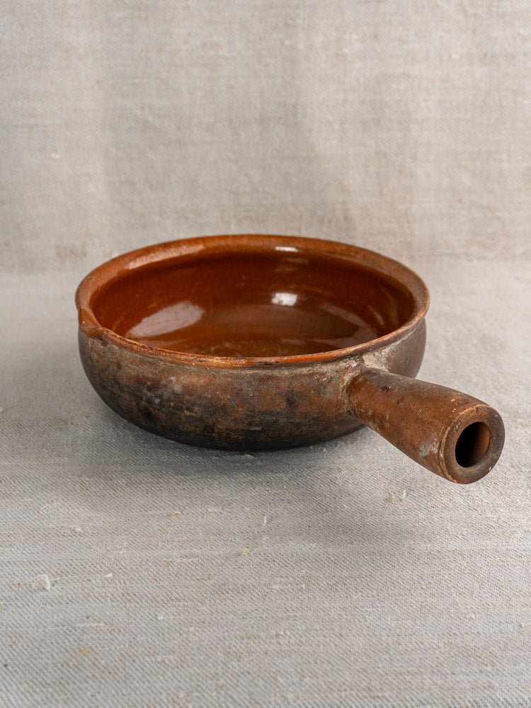 Antique French Saint-Uze stoneware cooking pan in rustic brown on textured beige fabric.