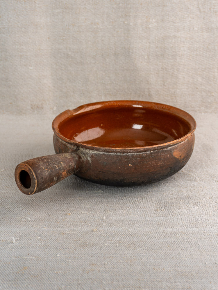 Antique French Saint-Uze stoneware poêlon with glossy interior and rustic brown matte exterior on beige fabric.