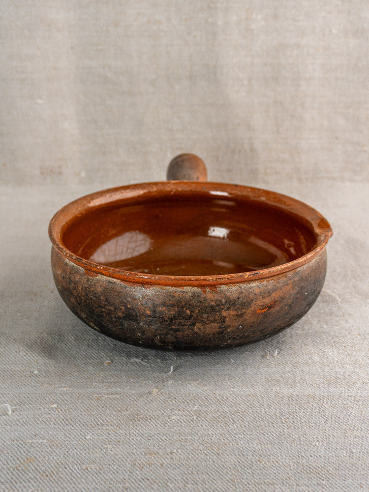 Antique French Saint-Uze stoneware poêlon pan with brown ceramic finish, handle, and spout on light gray fabric.