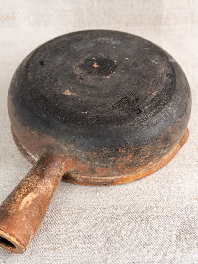 Antique French Saint-Uze stoneware poêlon displayed upside down, highlighting its worn base and robust handle.