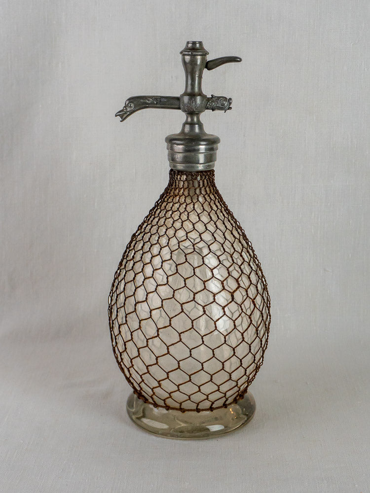 Antique French seltzer bottle with metal spout in a brown wire mesh cover.