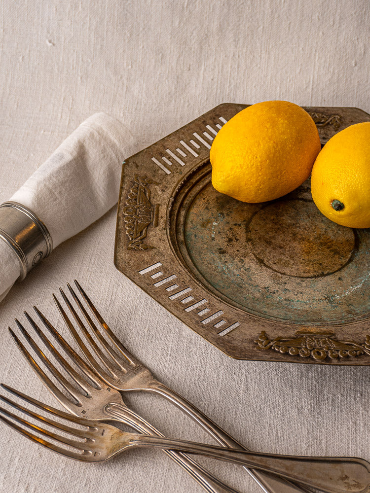 Art Deco French silver plate tazza with two lemons, napkin in silver ring, and vintage forks on beige tablecloth.