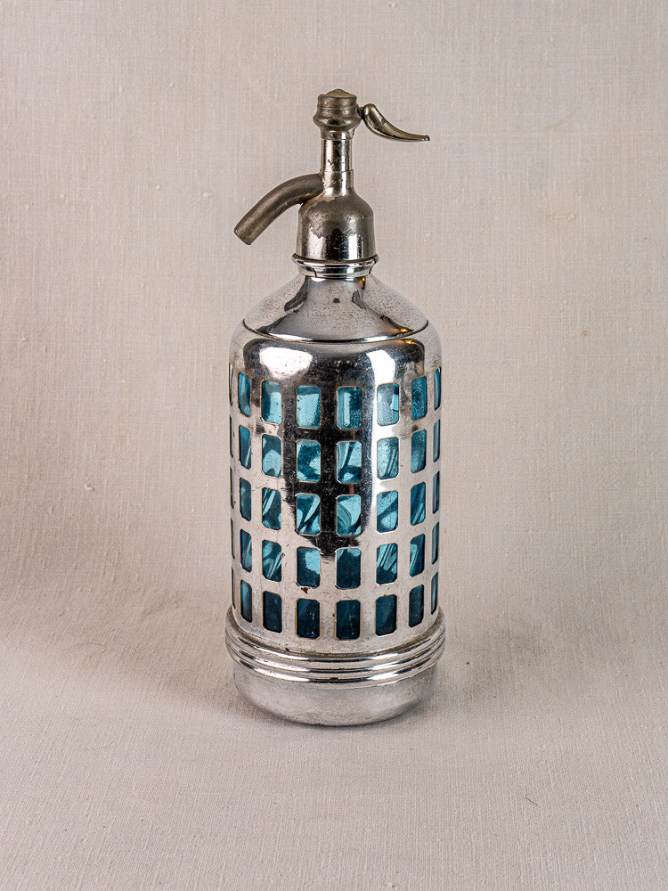 Antique French soda siphon with blue glass and silver metal top on neutral fabric, Paris bistro style.