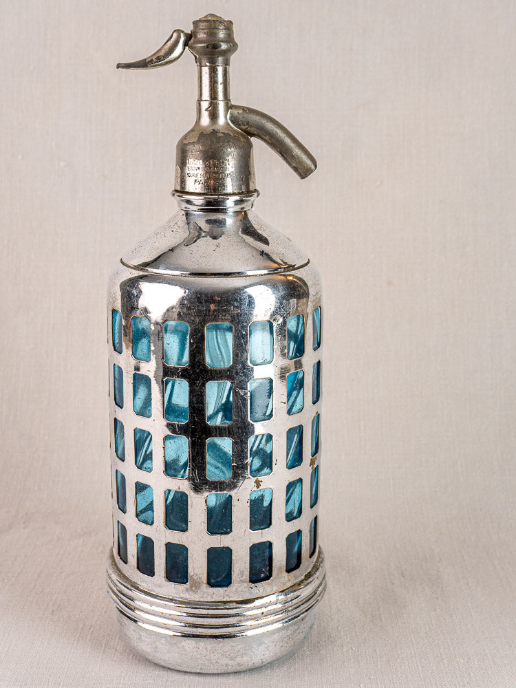 Antique French soda siphon with metal top, silver lattice casing, and blue-tinted glass, on a plain light background.