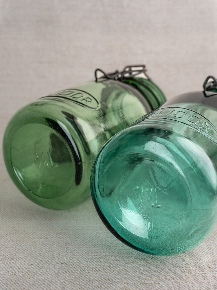Antique French Solidor and Durfor preserve jars in light green and aqua with metal clasps, embossed bases on neutral fabric.