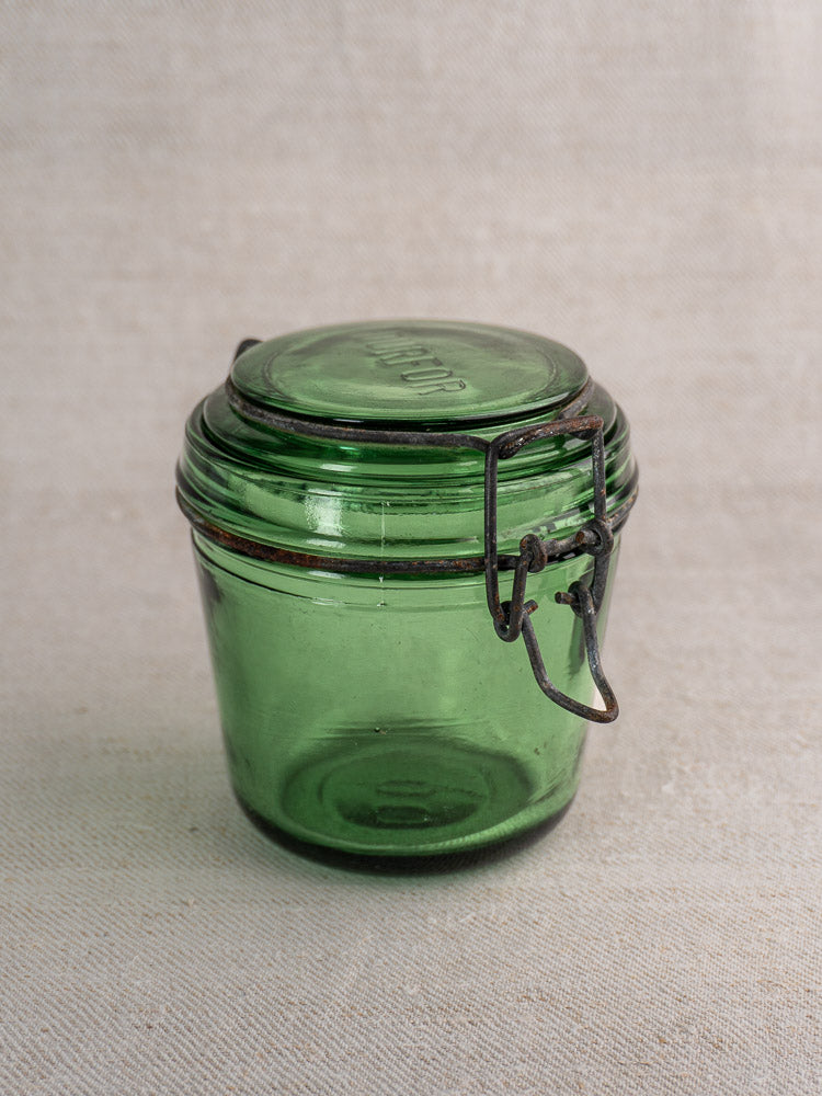 Set of three antique French Solidor & Durfor preserve jars with green glass, metal clasps, and lids on neutral fabric.