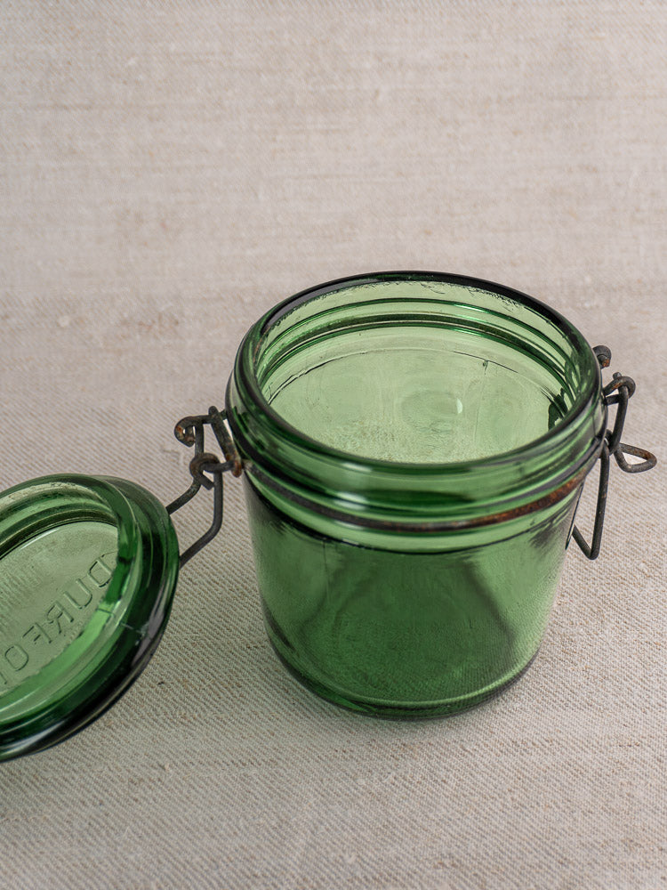 Antique French Solidor green preserve jar with hinged flip-top lid, open on a beige fabric surface.
