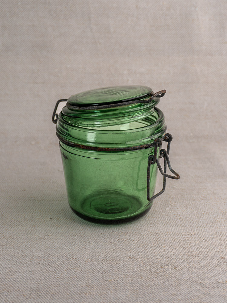 Antique French Solidor & Durfor green glass preserve jar with hinged metal clasp lid, set of three on beige surface.