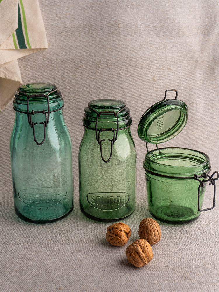 Set of three Antique French Solidor & Durfor preserve jars on fabric with three whole walnuts in front.