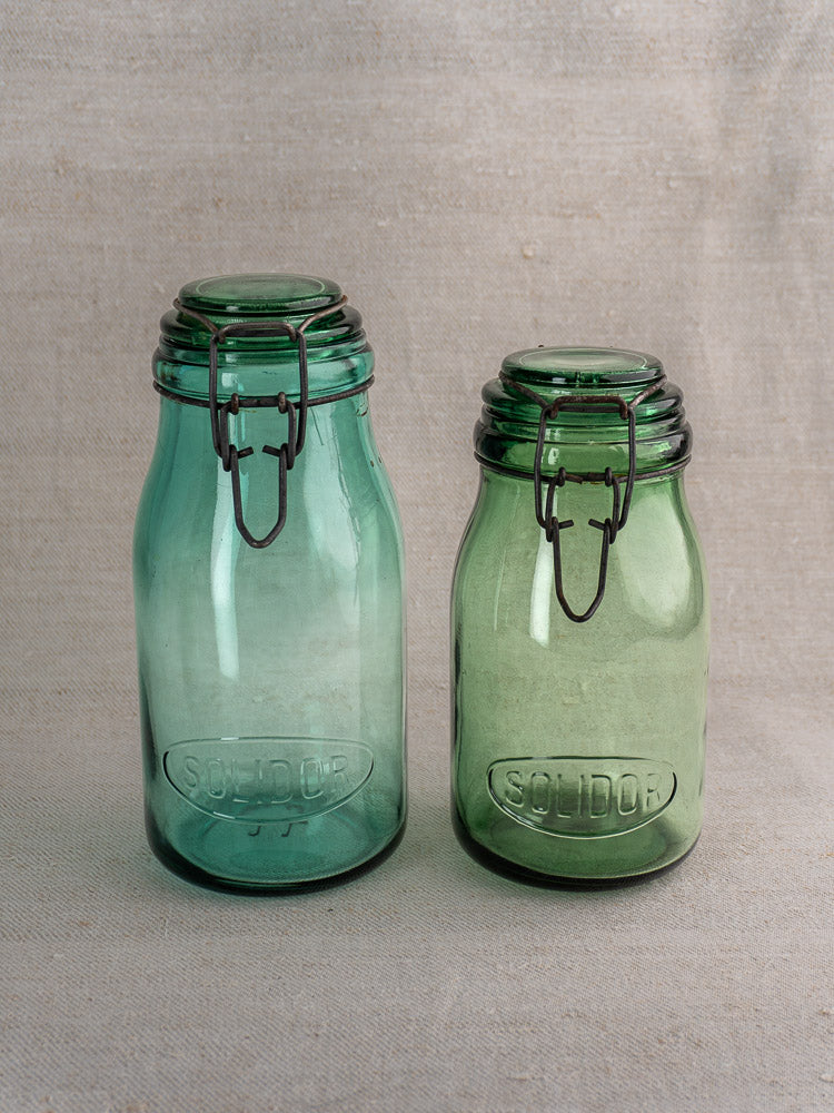 Antique French Solidor and Durfor green glass preserve jars with metal clasp lids, arranged on beige fabric.