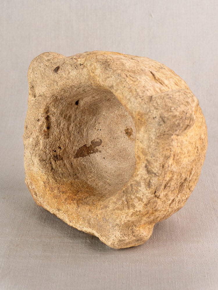 19th-century French stone mortar and pestle with deep oval bowl on a neutral gray fabric background.