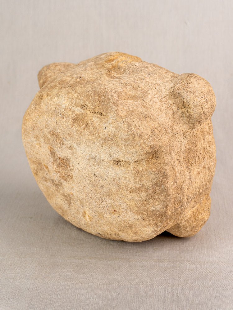 Antique French stone mortar with pestle, hand-carved, rounded shape and four knobs on a neutral surface.