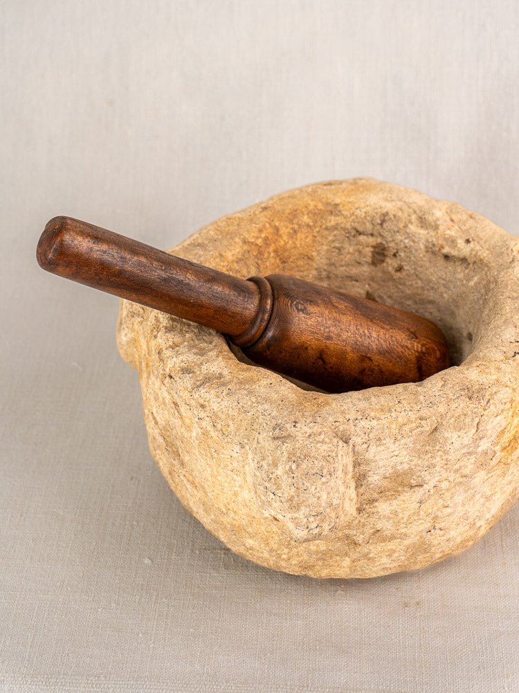 Antique French stone mortar and pestle with hand-carved Provençal design, wooden pestle, neutral textured backdrop.