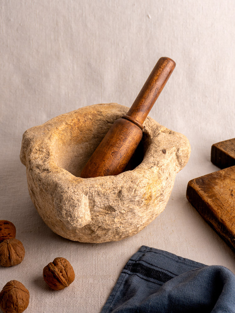 Antique French hand-carved stone mortar and wooden pestle displayed on a neutral gray surface.