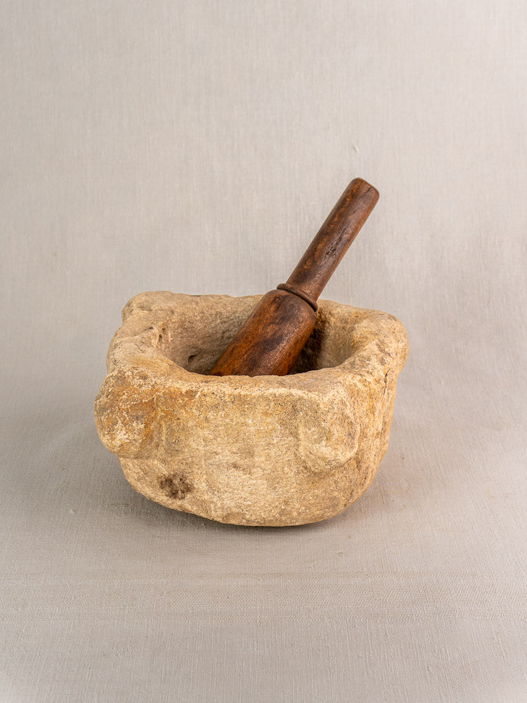Antique French hand-carved stone mortar and wooden pestle displayed on a neutral gray surface.