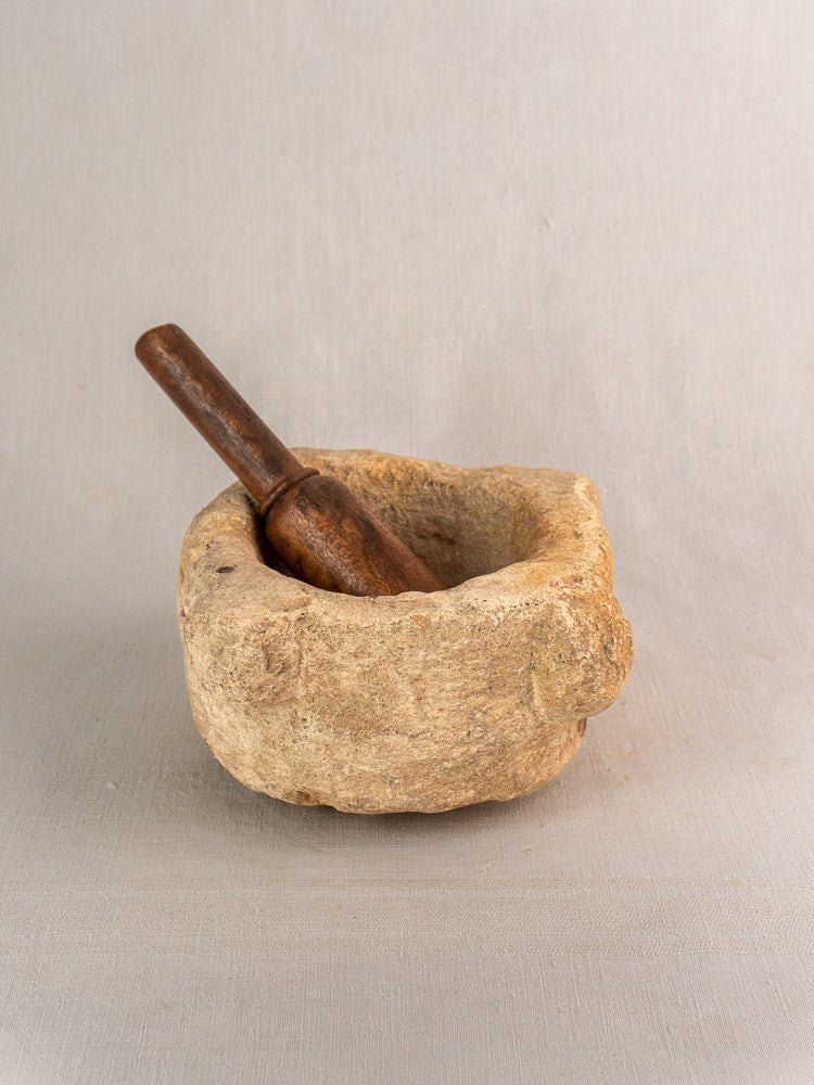 Antique French limestone mortar and dark wood pestle on light gray fabric with neutral background.