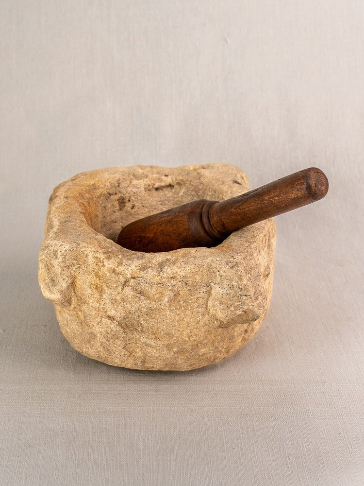 Antique French limestone mortar with wooden pestle, hand-carved Provençal 19th-century mortier on light gray surface.