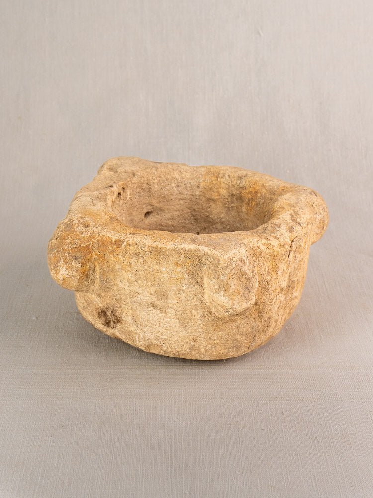 Antique French stone mortar and pestle, 19th-century Provençal mortier with irregular edges, on light gray background.