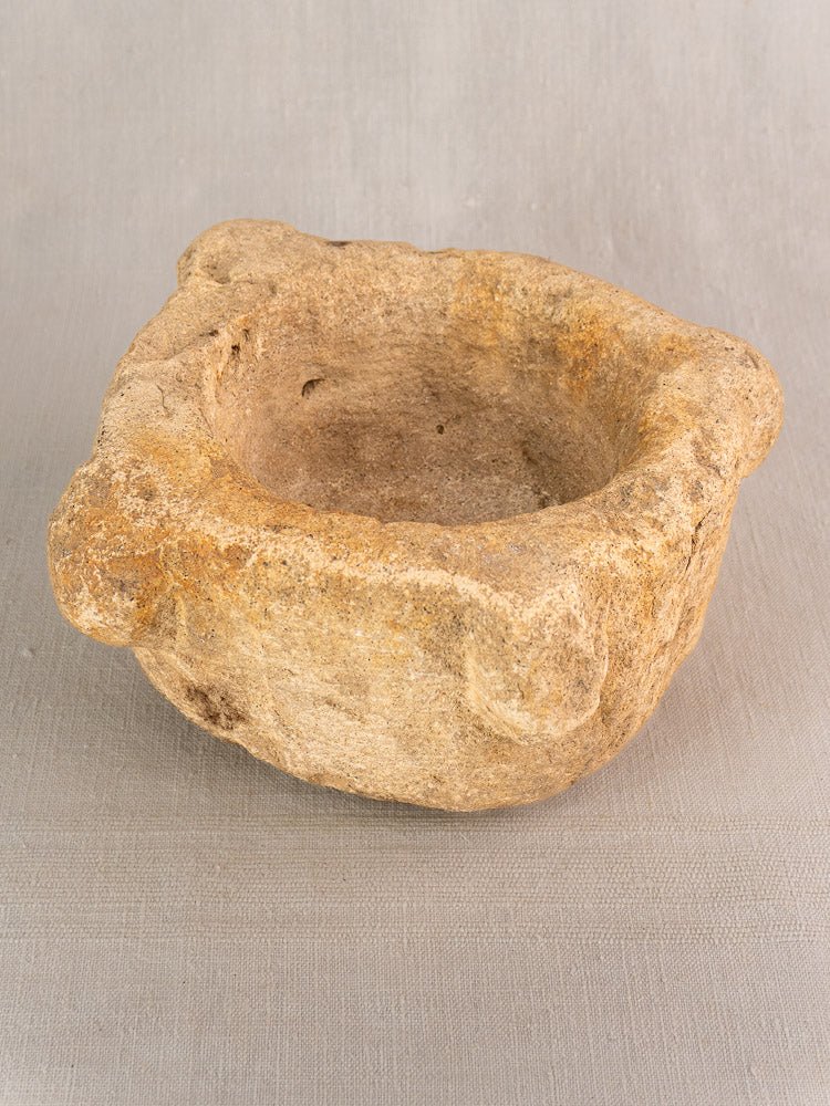 Antique French limestone mortar and pestle, 19th-century Provençal style, on neutral fabric background.