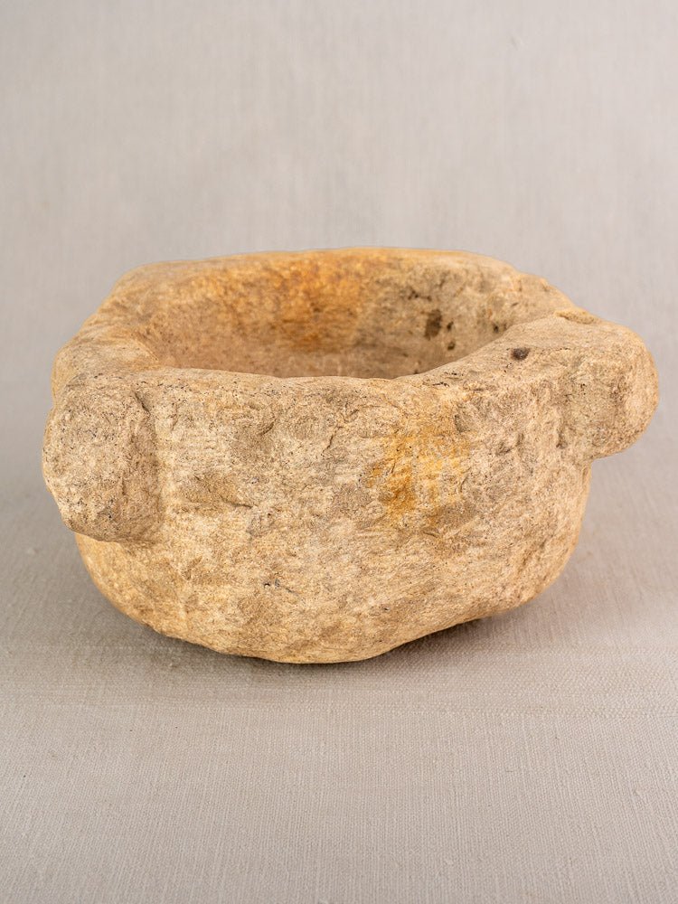 19th-century French stone mortar and pestle with rustic edges, displayed on light gray fabric against a neutral backdrop.