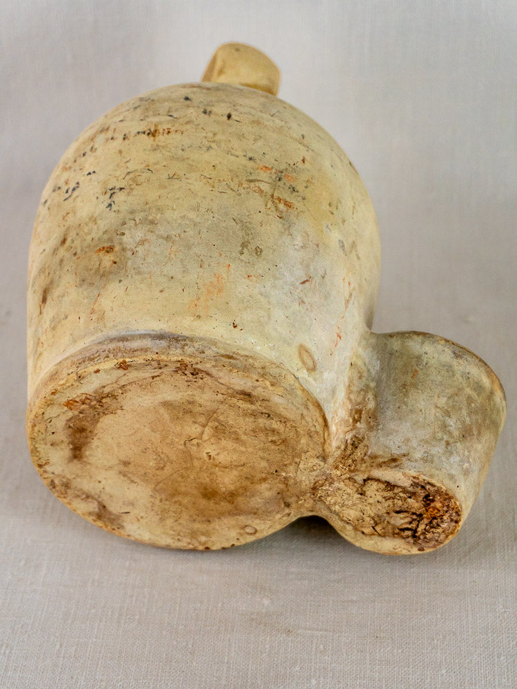 Antique French stoneware bird waterer with rounded base and side spout on neutral fabric.