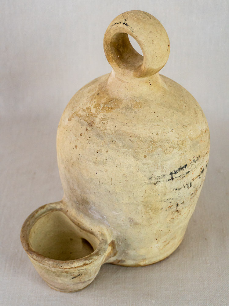 Antique French stoneware bird waterer with looped handle and attached base cup on plain background.