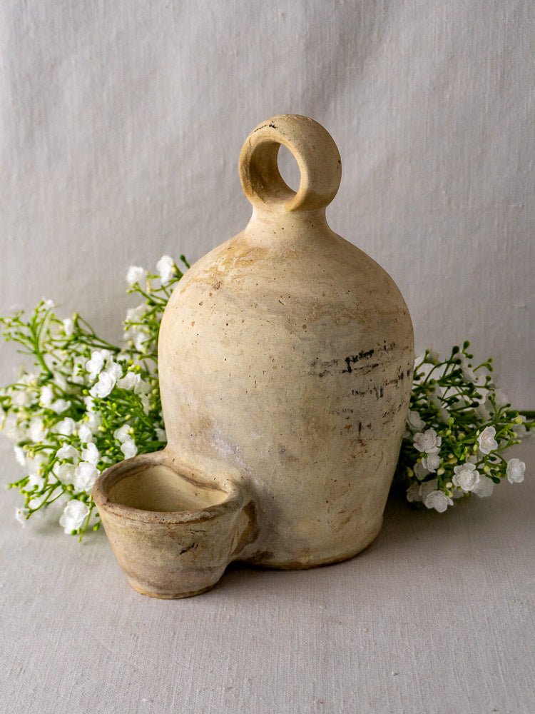 Antique French stoneware bird waterer in rustic beige ceramic with rounded bottle and shallow bowl.