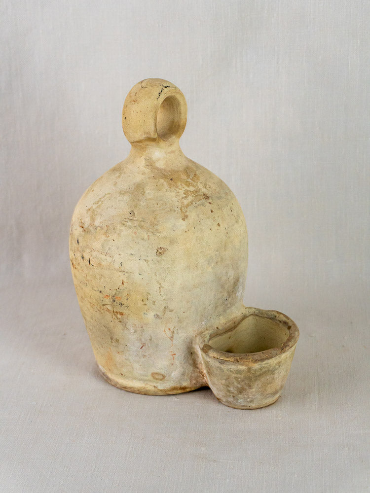 Antique French stoneware bird waterer in rustic beige ceramic with rounded bottle and shallow bowl.