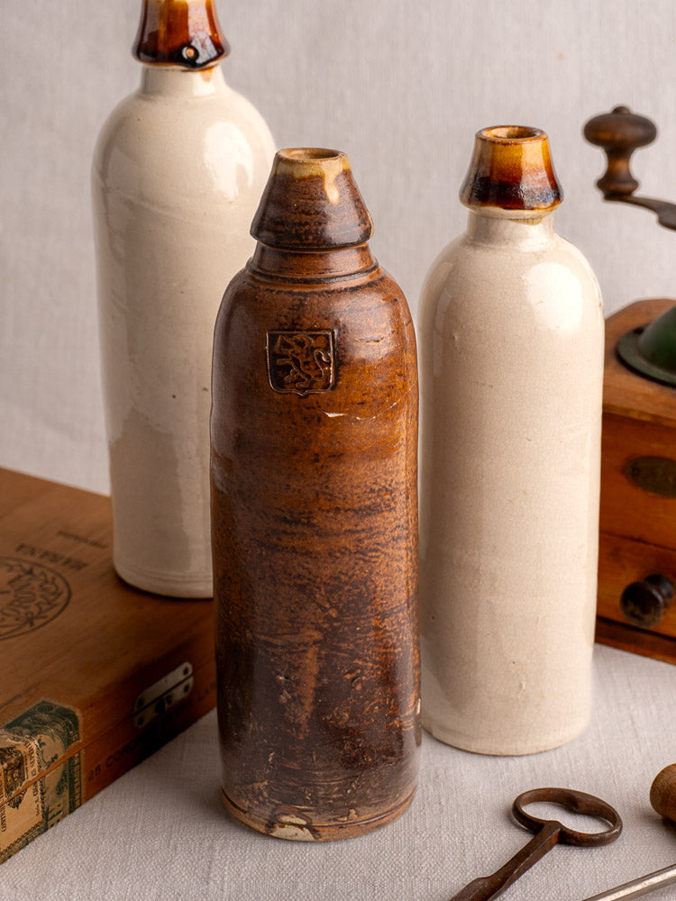 Set of three antique French stoneware cider and beer bottles with contrasting glazed finishes on gray fabric.