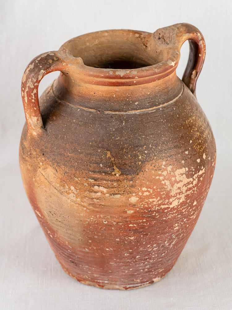 Early 19th-century French stoneware oil jug with ochre glaze, two handles, aged patina, plain background.