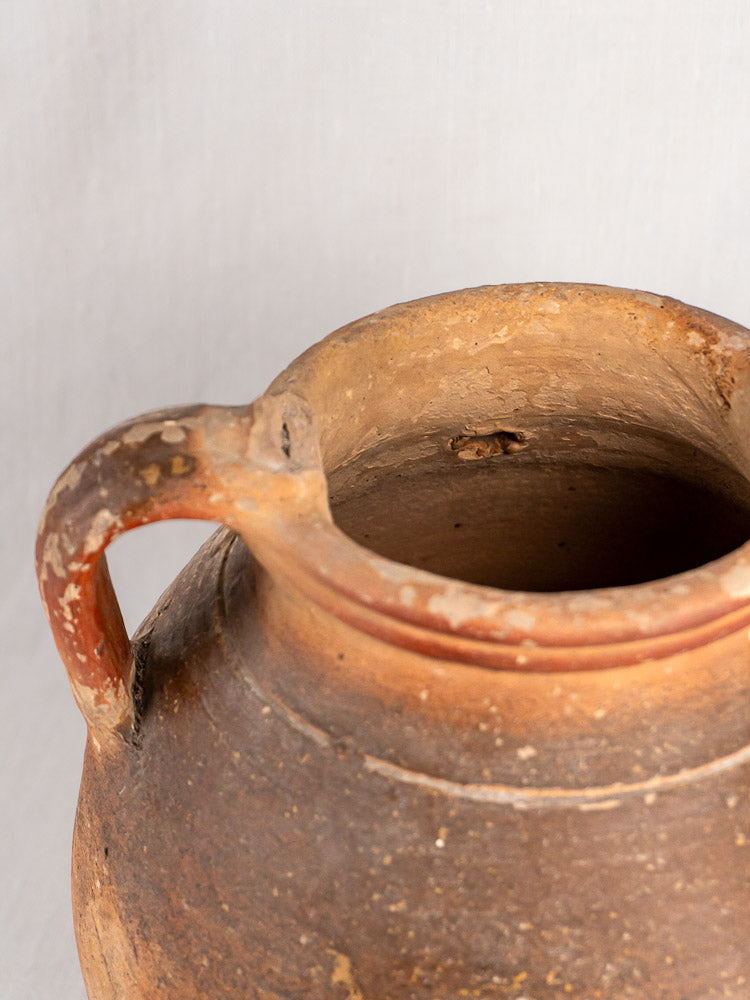 Antique French stoneware oil jug with ochre glaze, single handle, rough texture, wide mouth.