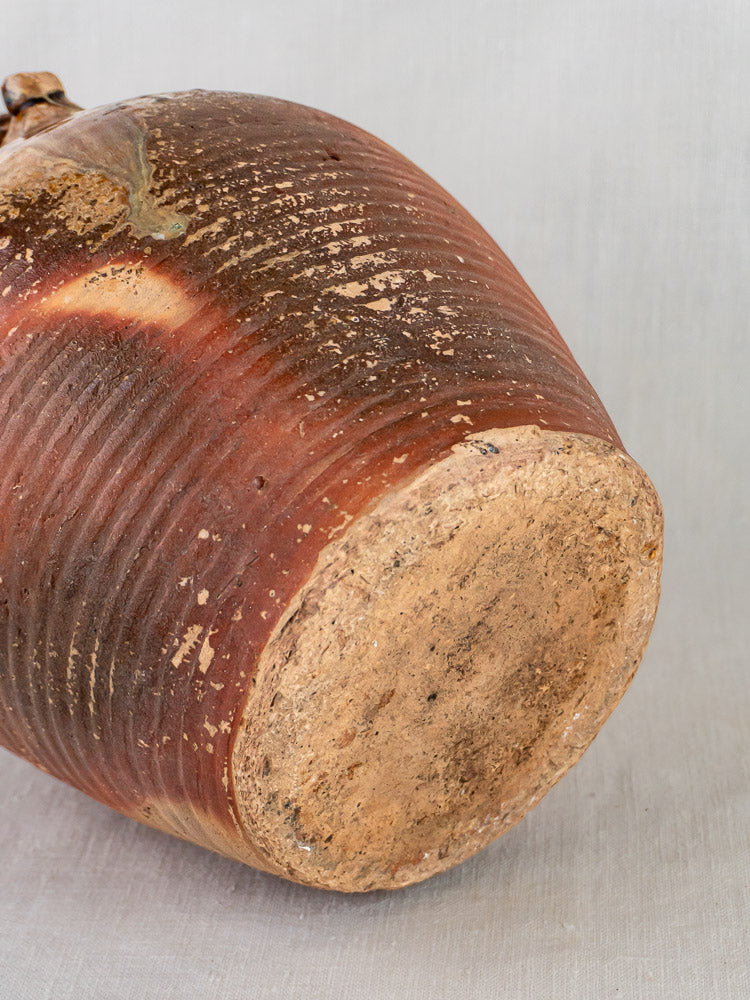 Antique French stoneware oil jug base with ochre glaze, ribbed texture, light gray background.
