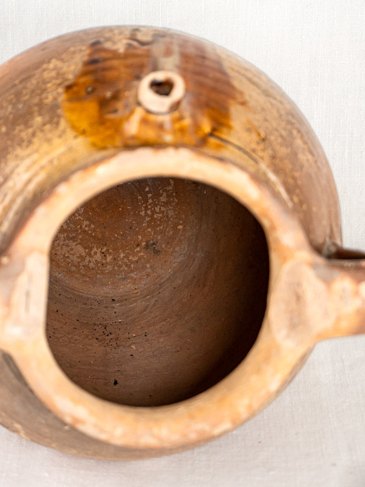 Antique French stoneware oil jug with ochre glaze, wide opening, and side spout on pale surface.