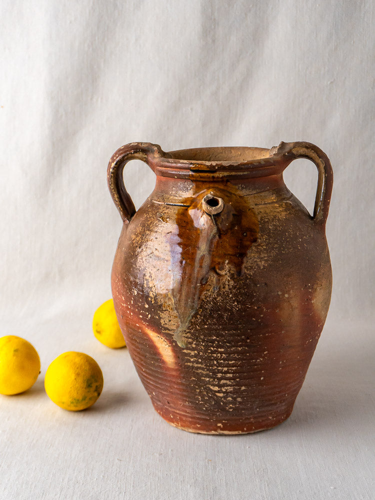 Antique French stoneware oil jug with ochre glaze and two handles, beside three lemons.