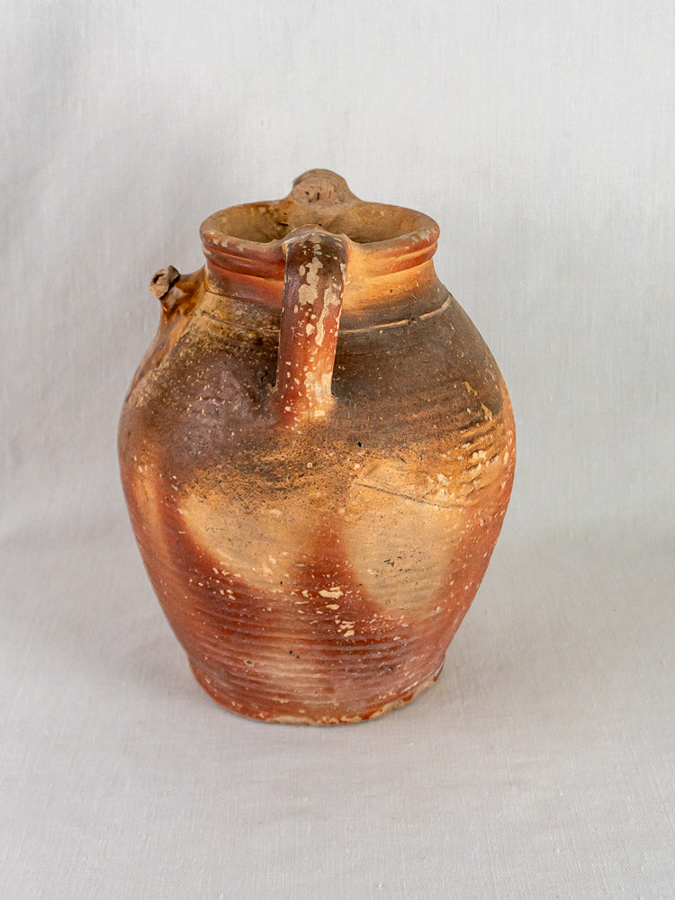 Antique French stoneware oil jug with ochre glaze, rustic brown finish, and single handle.