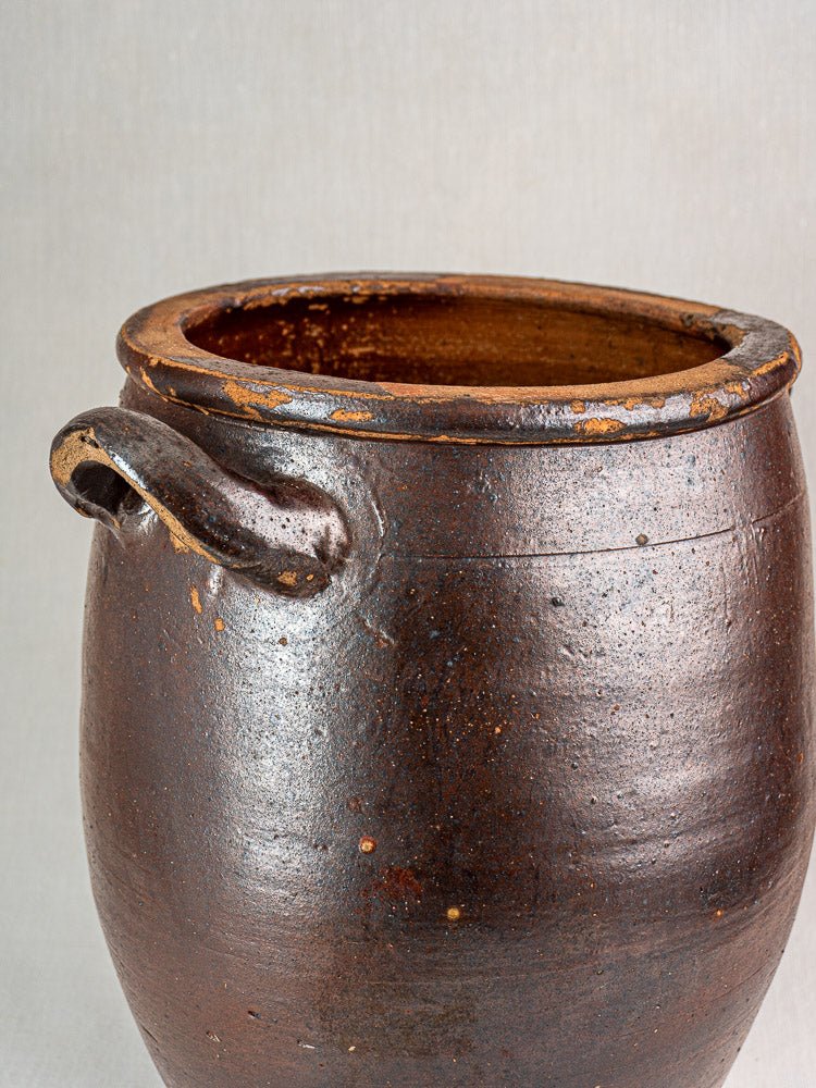 Antique French salt-glazed stoneware storage jar with single handle and textured dark brown surface.