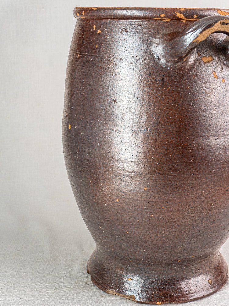 Antique French salt glazed stoneware storage jar with handle, textured surface, and rim chips on light background.