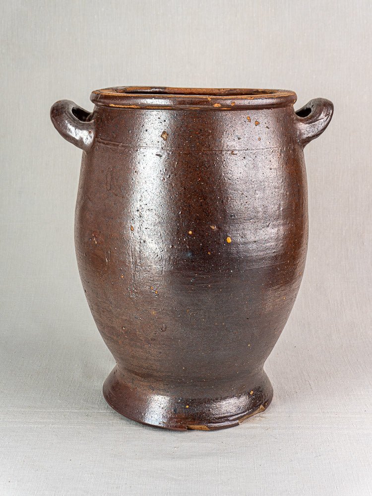 Antique French salt-glazed stoneware pot à graisse with brown glaze and two side handles on gray surface.