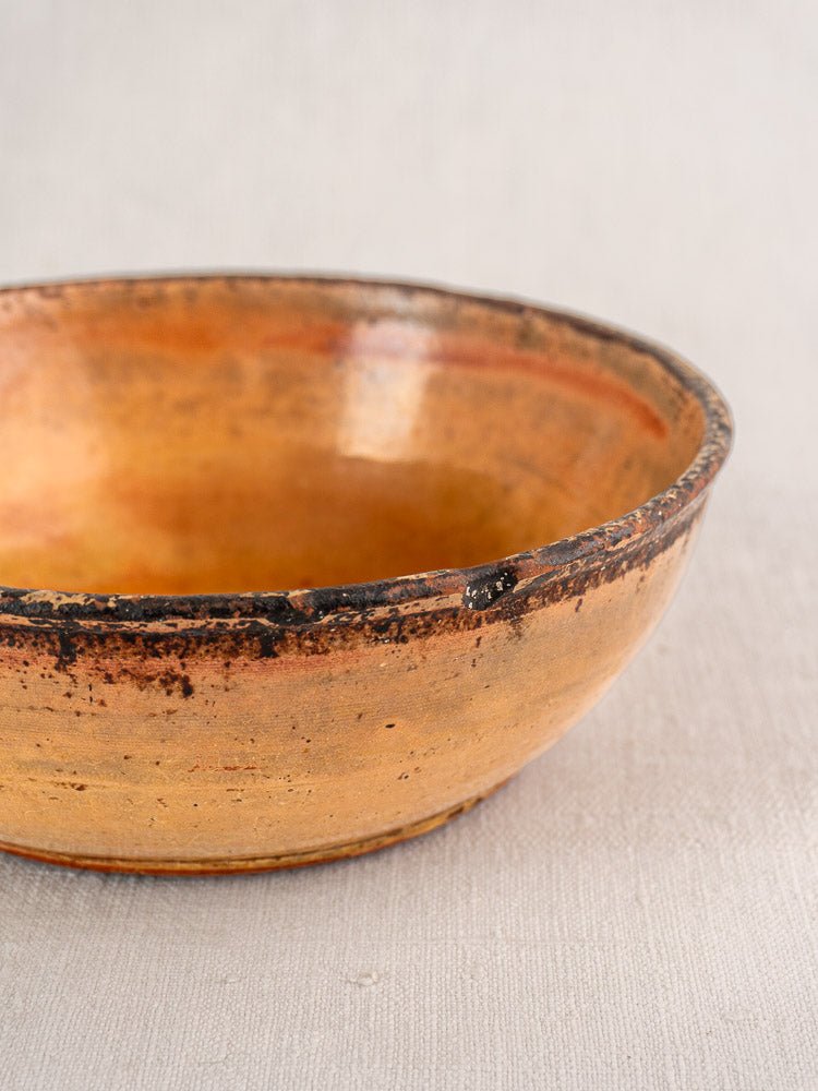 Antique French yellow earthenware Tian baking dish with weathered rim on a light fabric surface.