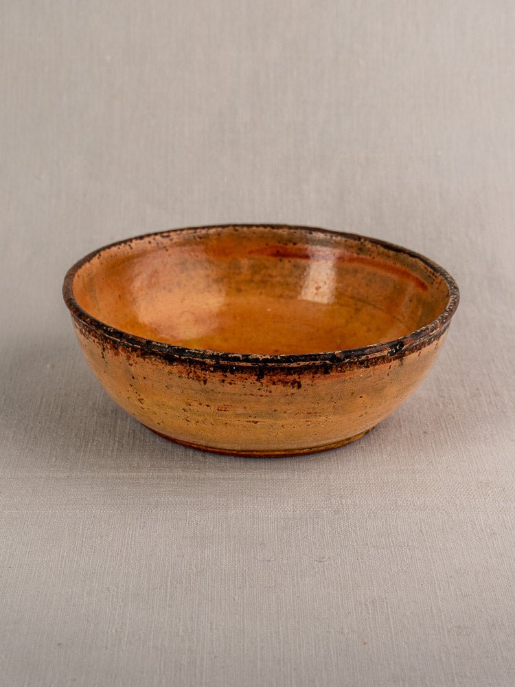 Antique French Tian baking dish in yellow glazed earthenware with uneven rim on light gray fabric.