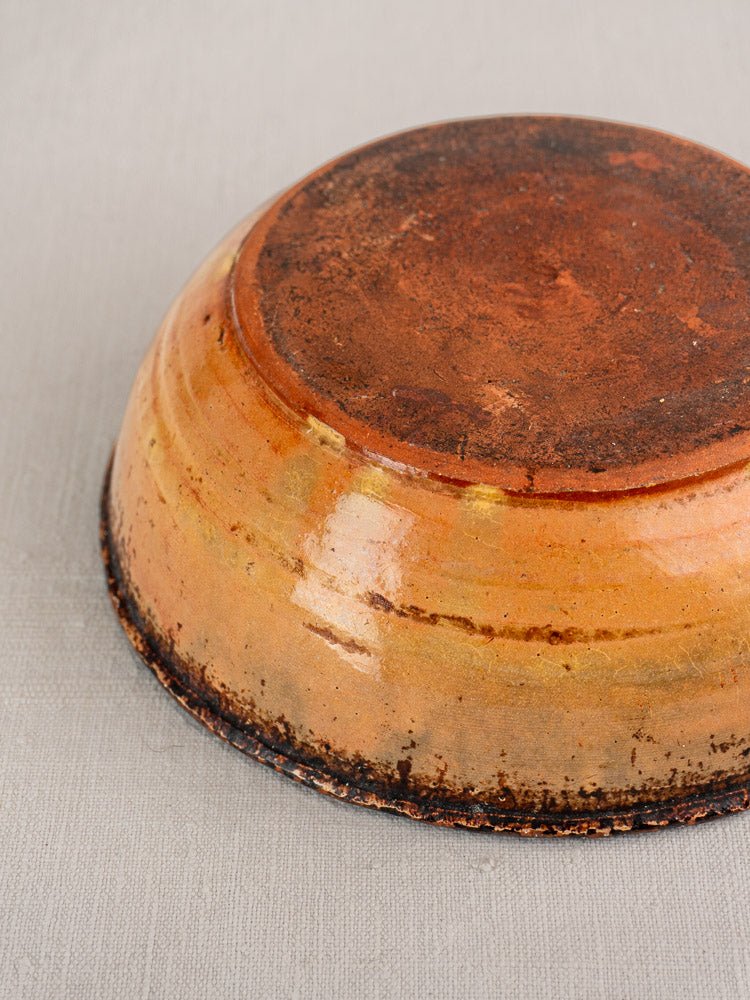 Antique French Tian baking dish in yellow glazed earthenware, upside down on a light gray surface.
