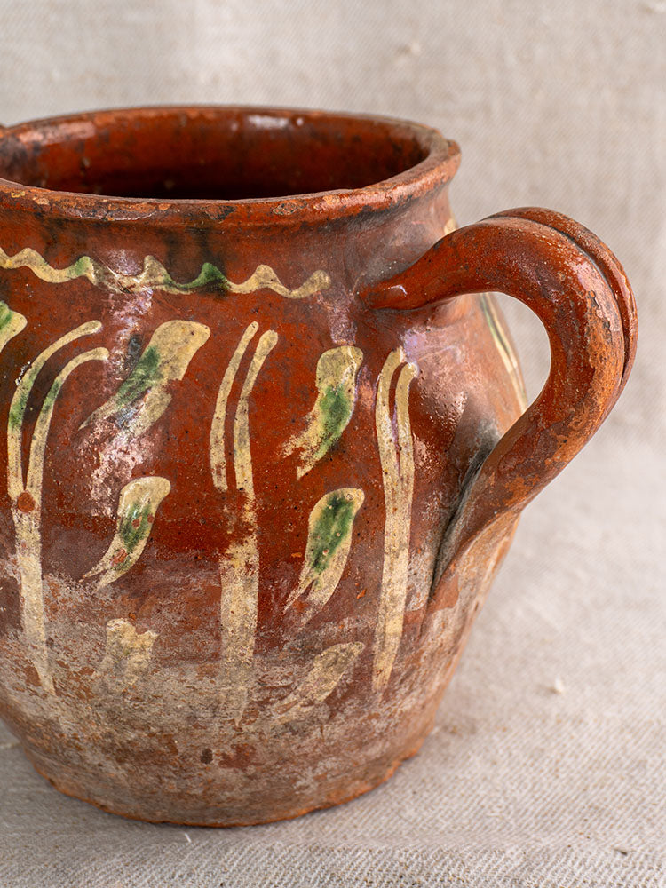 Early 19th-century French terracotta pot with handle, jaspé slipware cream and green décor, aged patina, on beige fabric.
