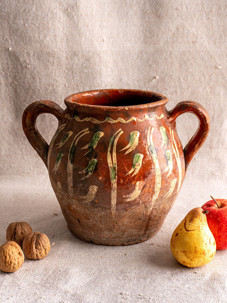 French terracotta pot with Jaspé décor, slipware, twin handles, cream and green patterns on beige fabric background.