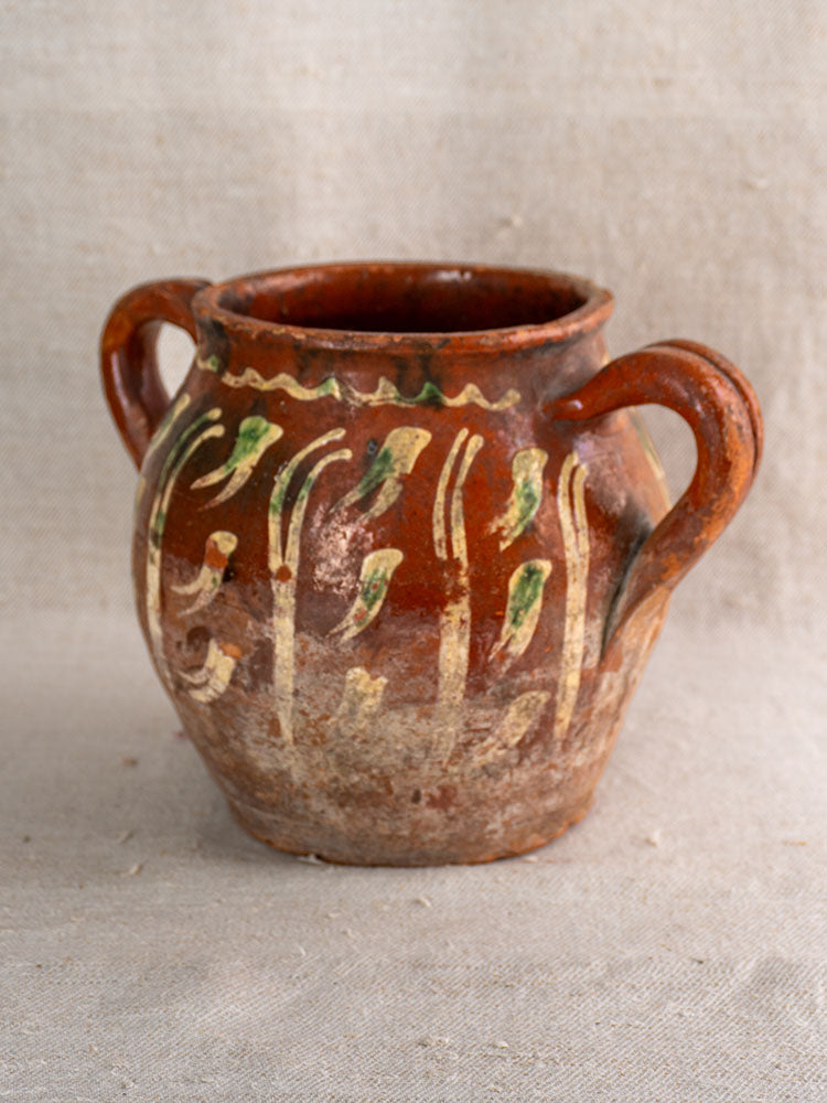 French terracotta pot with Jaspé décor, slipware, twin handles, cream and green patterns on beige fabric background.
